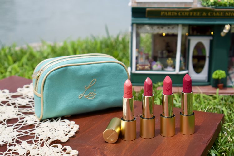Lisa Eldridge Summer Pinks Collection Lipstick and Cosmetic Bag Display with Miniature House and Lake in Background